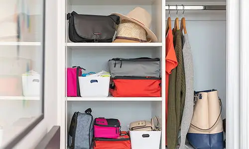 Labeled packing cubes on a closet shelf for seasonal clothing.